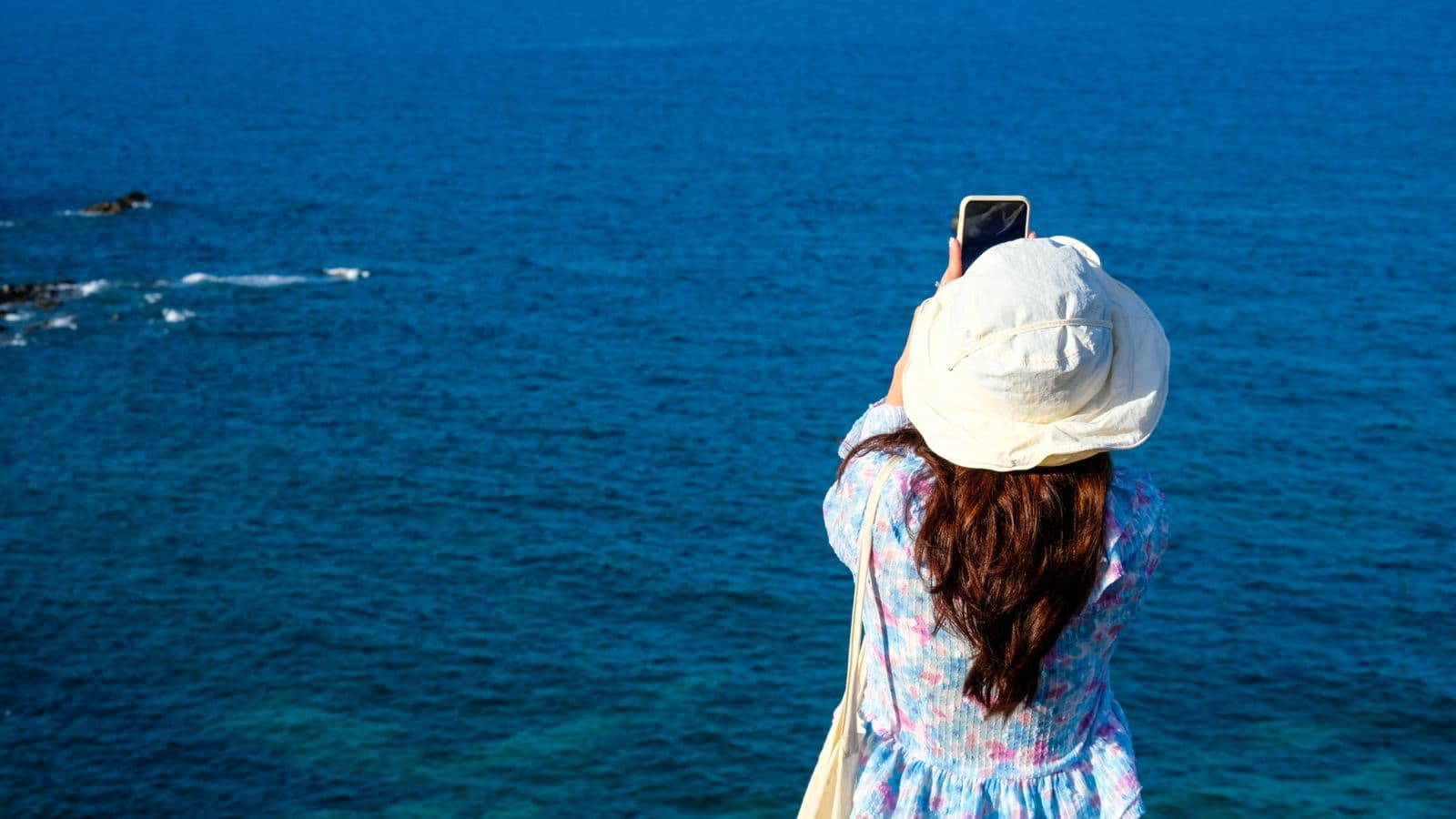 Content creator in a summer hat filming the sea with her smartphone