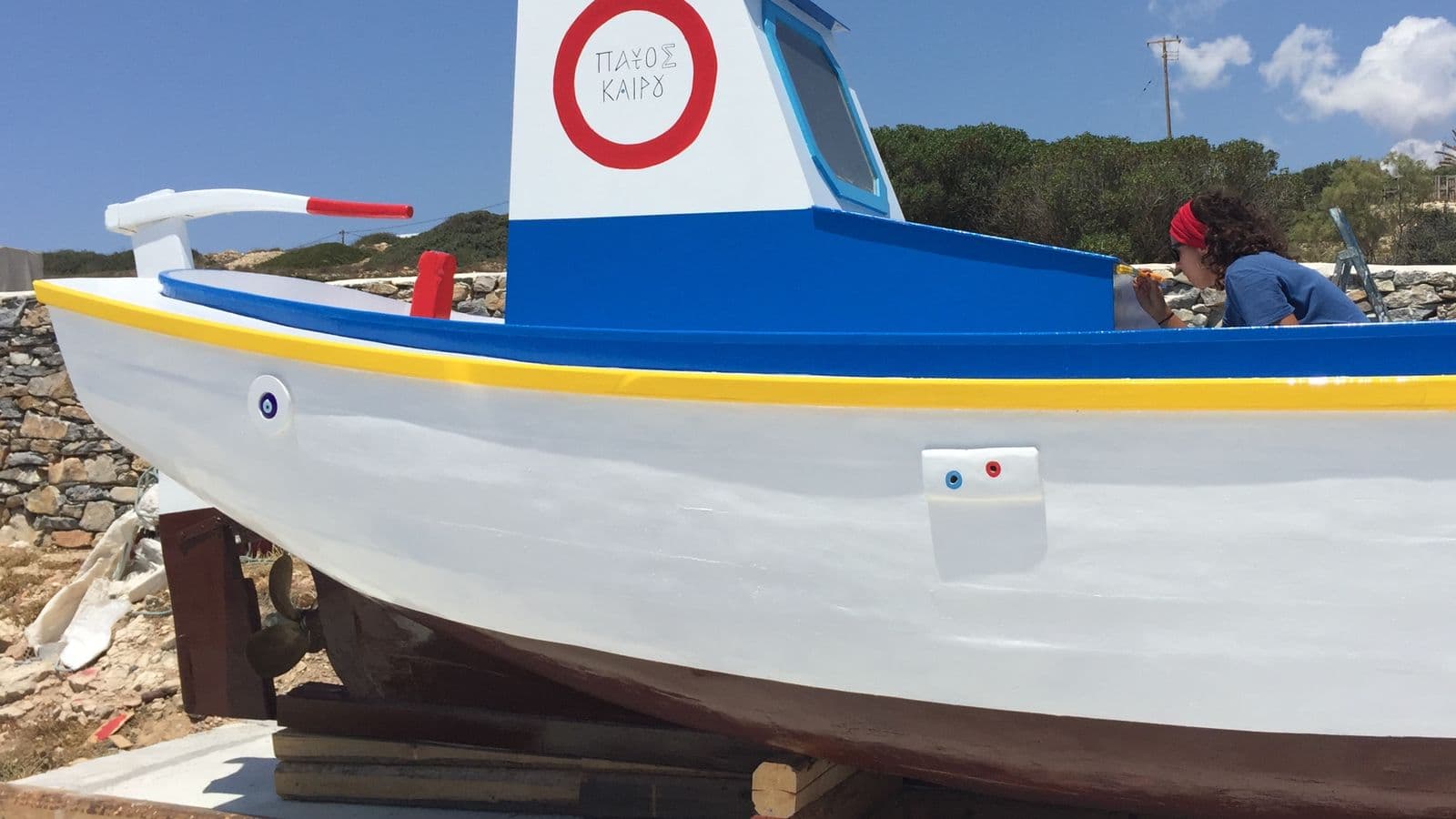 Γυναίκα που βάφει ένα μπλε και λευκό ψαροκάικο στη Νάξο κάτω από καθαρό ουρανό